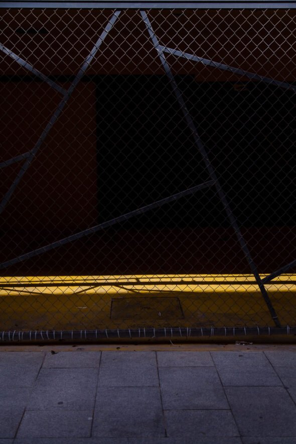 A dark view through a fence onto with natural light shining onto a yellow floor