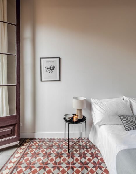 Single bedroon with natural light. framed wall picture, white bedding, small side table and large french door to terrace