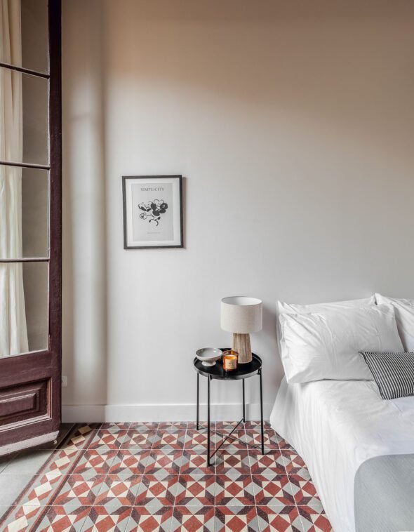 Single bedroon with natural light. framed wall picture, white bedding, small side table and large french door to terrace