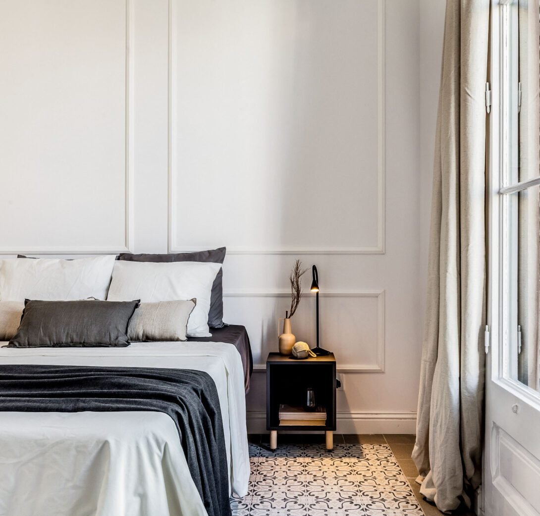 Modern and chic eixample residence decorated in black and white bedding, bedside table, balcony door and warm lighting