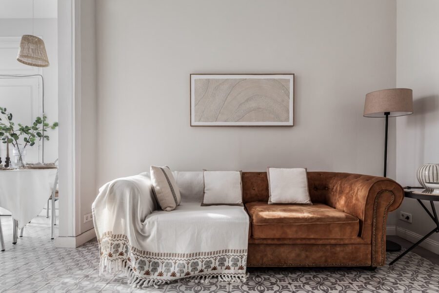 Large faux tan leather sofa draped in a beige throw, wall art and lamp next to the dining area all photographed in naturally golden lighting