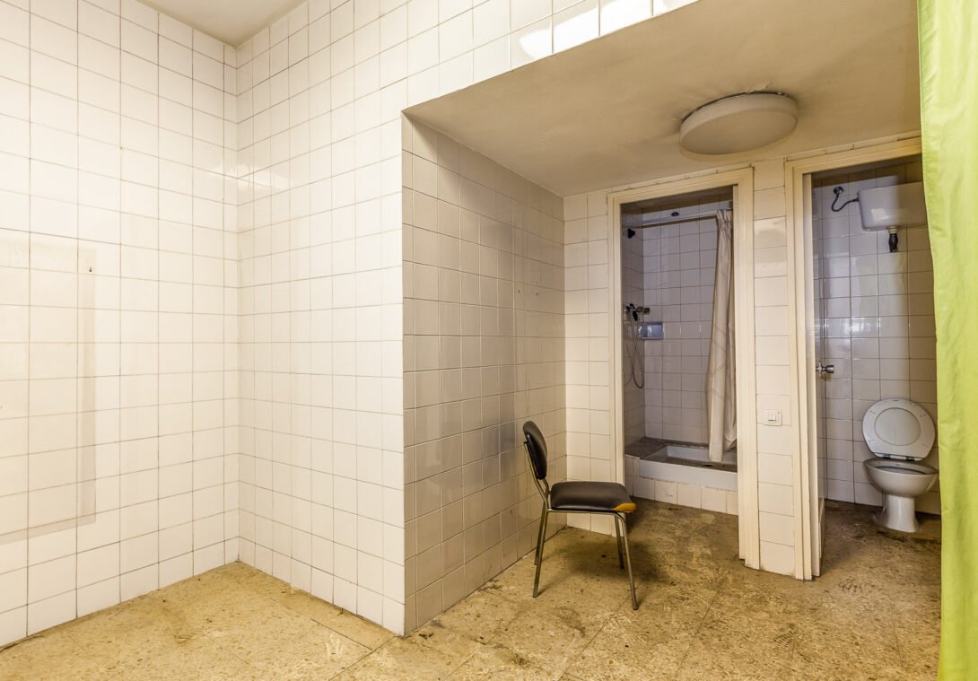 Abandoned factory bathroom with chair, shower and toilet rooms