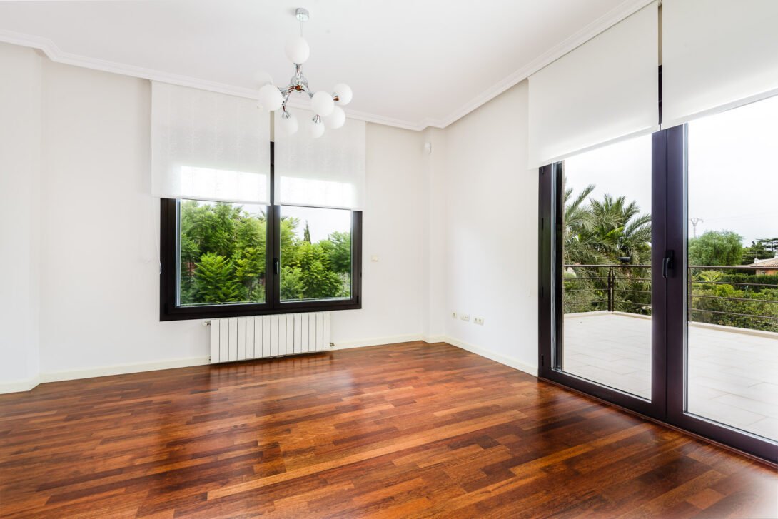 Empty bedroom with wooden floors, a window and french doors with view to very green pine trees