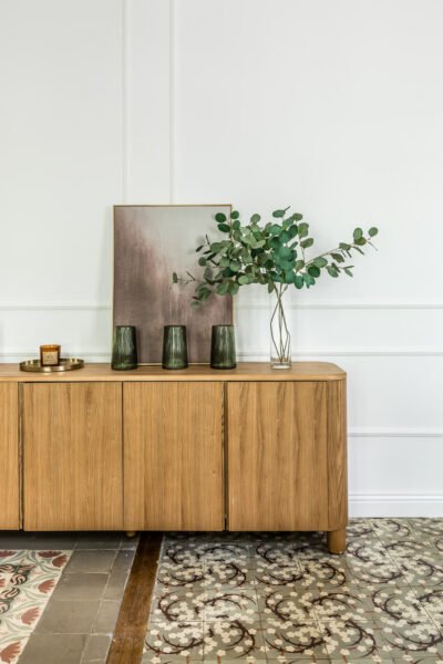 A long wooden mid century style cabinet decorated with an abstract painting, vases, candles and dried eucalyptus stems for interior design.