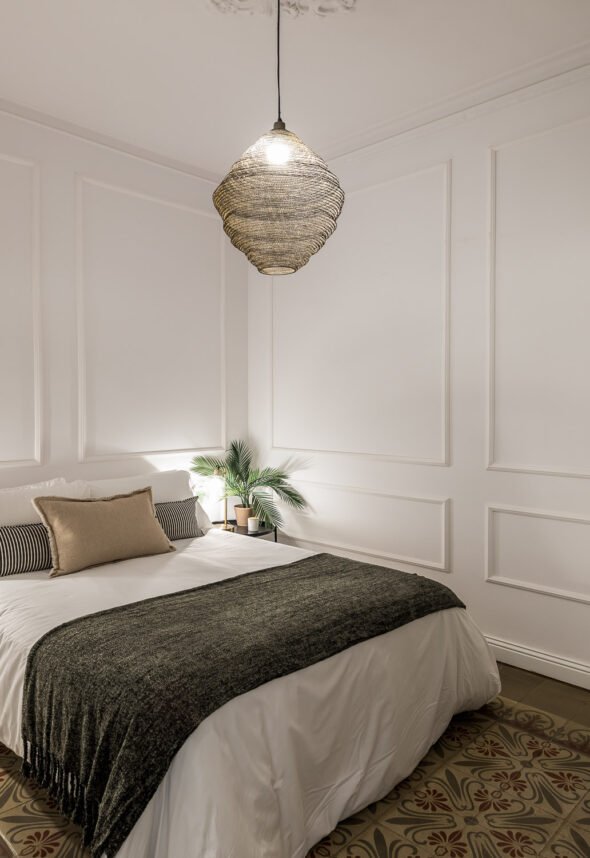 A bedroom with a beehive styled lampshade hanging from a ceiling a bed dressed with white linen and a black throw for residential interior design.