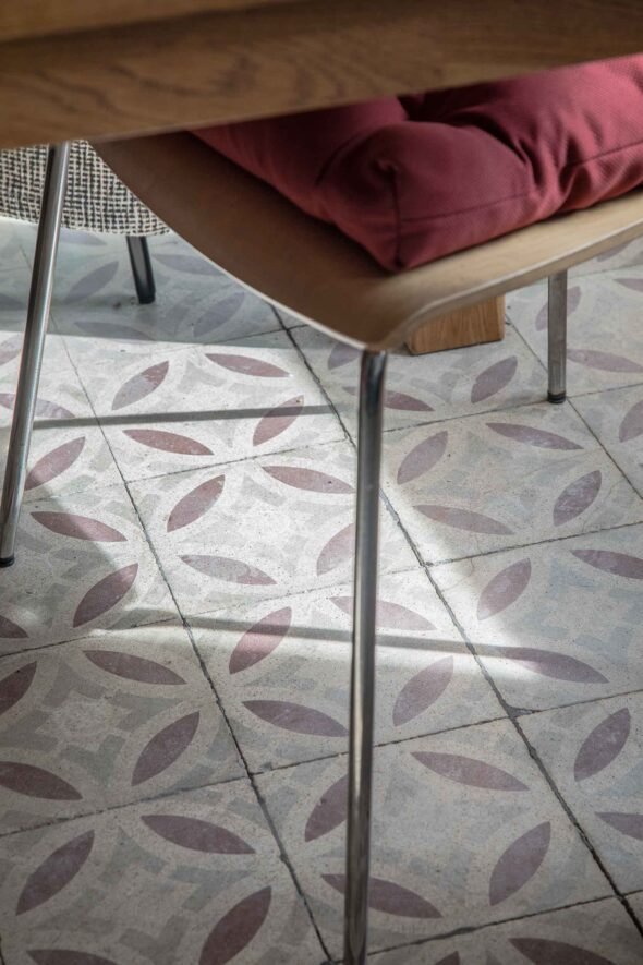 A wooden chair with a dark red cushion and metal leg and mosaic tiles with red and grey pattern.