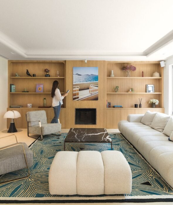 Beautifully styled mid century modern living room with pipistrello lamp, large wooden wall book shelf unit, marble table and boucle modula sofa, with model for interior design magazine.