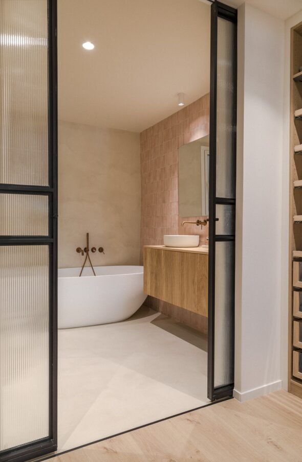bathroom with baby pink tiles, natural wooden cabinetry and oval porcelain bath with bronze taps in a residential apartment in Barcelona