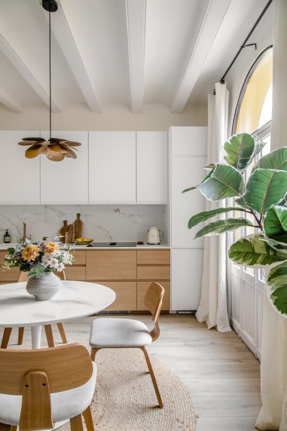Gorgeous natural light kitchen diner styled with a mix of scandinavian vibe and contemporary, consists of wooden cabinets and chairs and marble table and work tops with lots of colourful plants and flowers