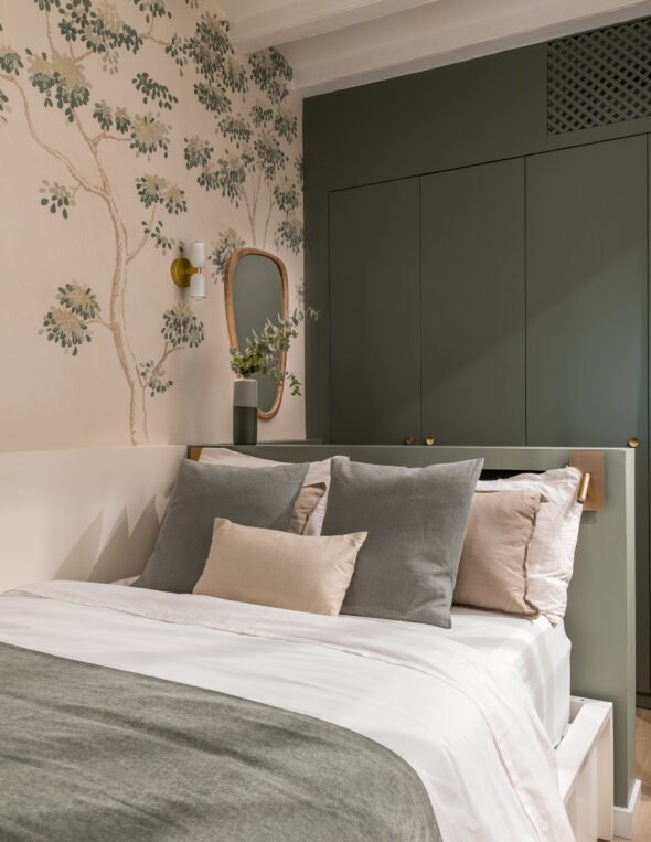 a bedroom with tones of olive greens for cabinets and bedding also walls adorned with wallpaper with tree and leaf print