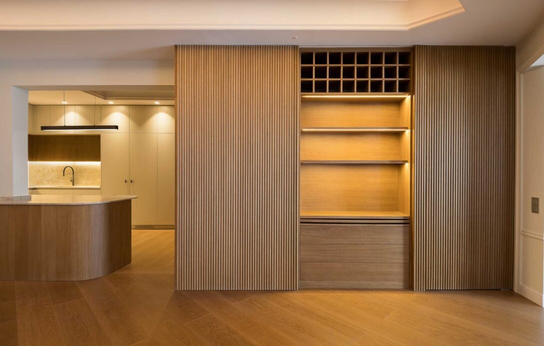 living room showcasing bespoke sliding wooden doors concealed sleeping zone adjacent to kitchen with warm lighting.