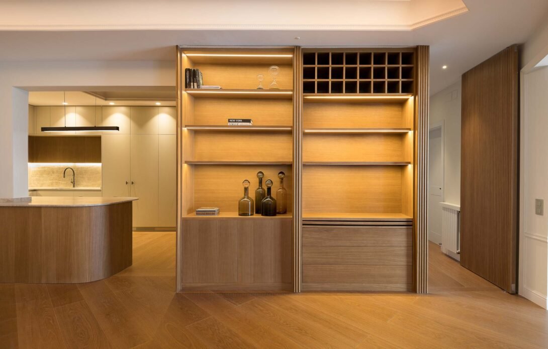 living room showcasing bespoke sliding wooden doors concealed sleeping zone revealed adjacent to kitchen with warm lighting.