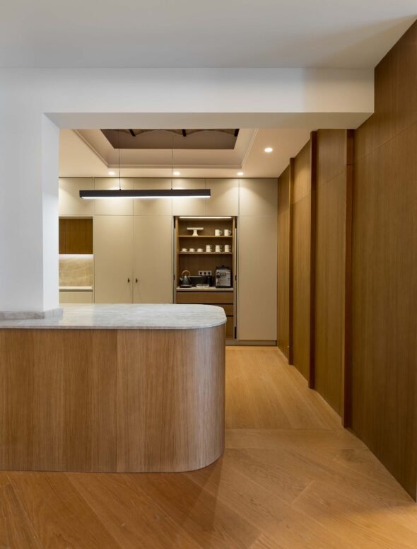 contemporary kitchen design with warm oat bespoke cabinets with pocket doors revealing coffee station, marble breakfast bar and suspended light fixture in the eixample barcelona.