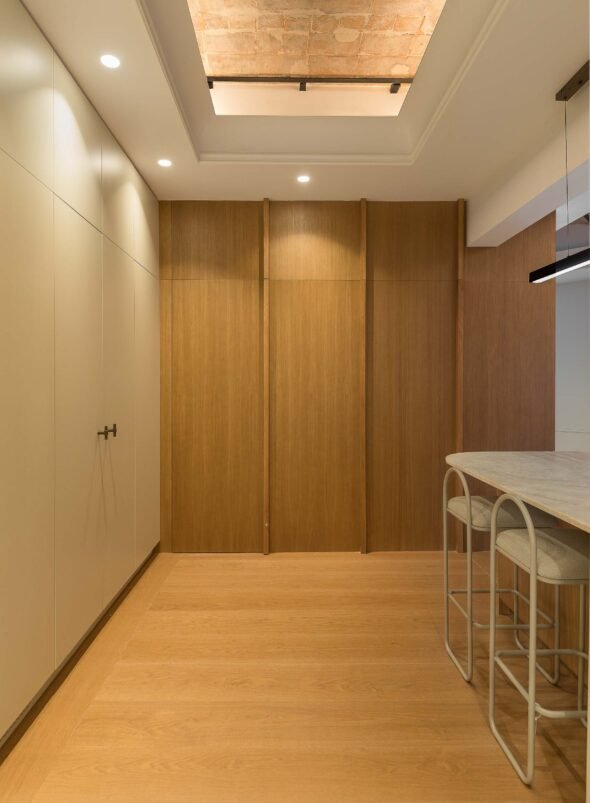 contemporary kitchen design with warm oat bespoke cabinets with pocket doors revealing storage, marble breakfast bar and suspended light fixture in the eixample barcelona.