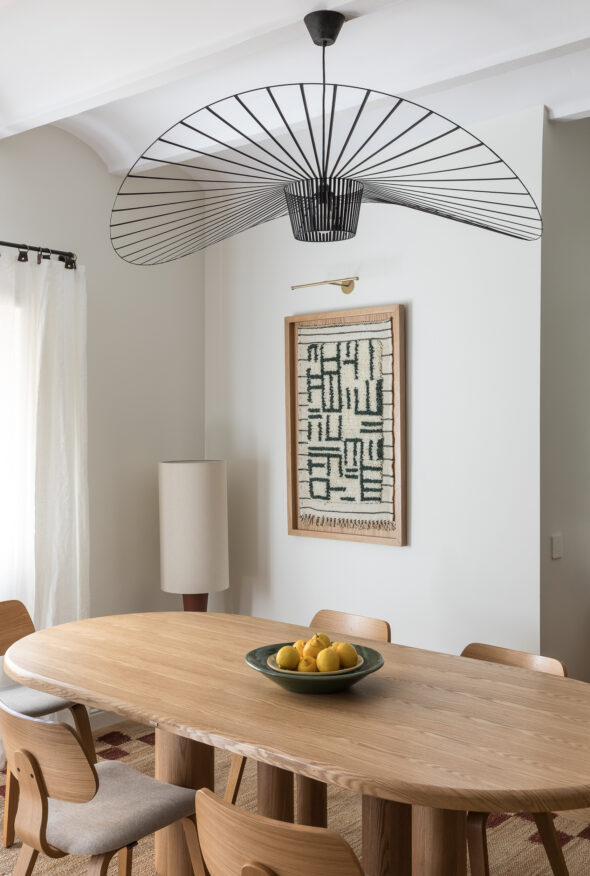Oblong bespoke wooden table and chairs, bowl of lemons featuring a large fan shaped pendant light over it. Natural and warm tones.