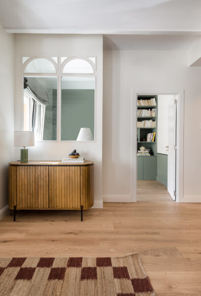 Wooden slatted modern cabinet set in a living room with a harlequin rug looking onto a home library, Very natural and warm tones of wood, burgandy and green in a newly refurbished apartment in Barcelona