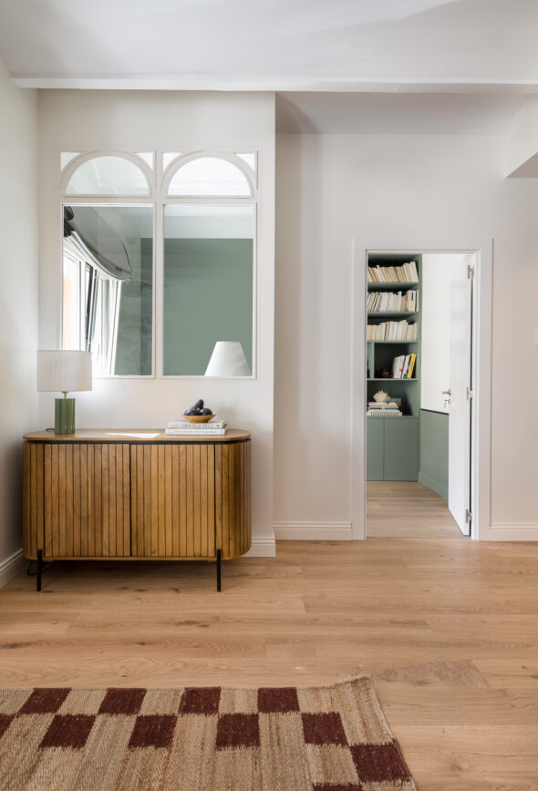 Wooden slatted modern cabinet set in a living room with a harlequin rug looking onto a home library, Very natural and warm tones of wood, burgandy and green in a newly refurbished apartment in Barcelona